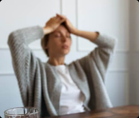 Vrouw zit met handen op haar hoofd aan tafel