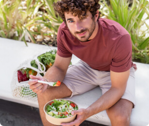 Man eet salade op een bankje in de buitenlucht