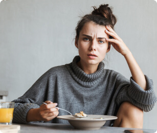 vrouw eet ontbijt aan tafel, maar heeft last van haar buik